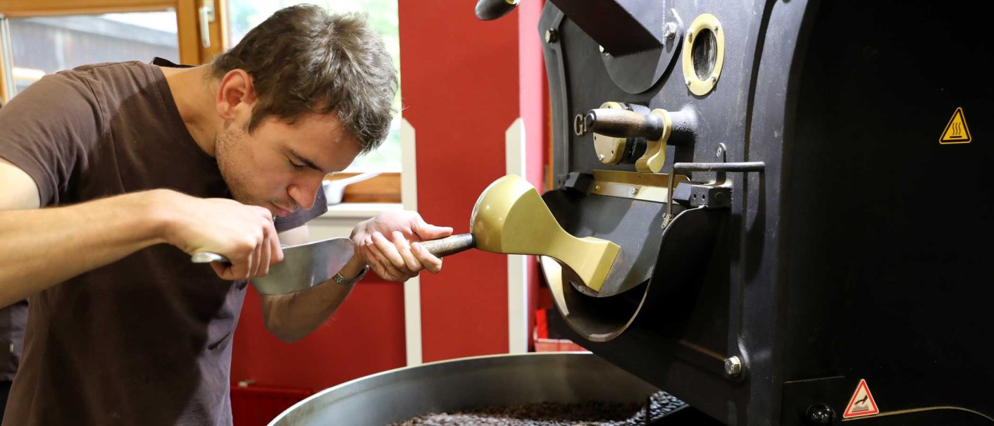 Ein Mann prüft den Duft von frisch gerösteten Kaffeebohnen in einer Röstmaschine. Er konzentriert sich auf das Aroma der Bohnen., © EINS + Alles/Christopherus e. V. Ein Mann prüft den Duft von frisch gerösteten Kaffeebohnen in einer Röstmaschine. Er konzentriert sich auf das Aroma der Bohnen., © EINS + Alles/Christopherus e. V.