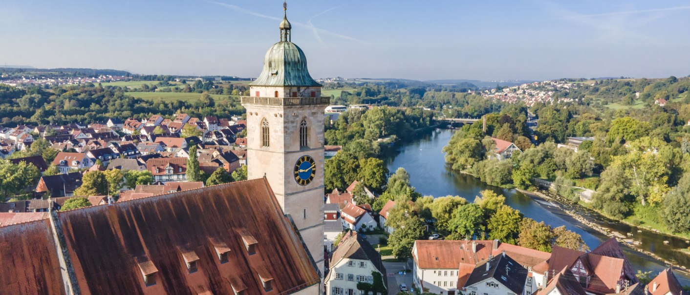 Drohnenansicht der Stadtkirche am Neckar, umgeben von roten Dächern und grüner Landschaft. Der Fluss schlängelt sich durch die Stadt., © Stadplanungsamt Stadt Nürtingen; artismedia GmbH/ Olaf Kühl