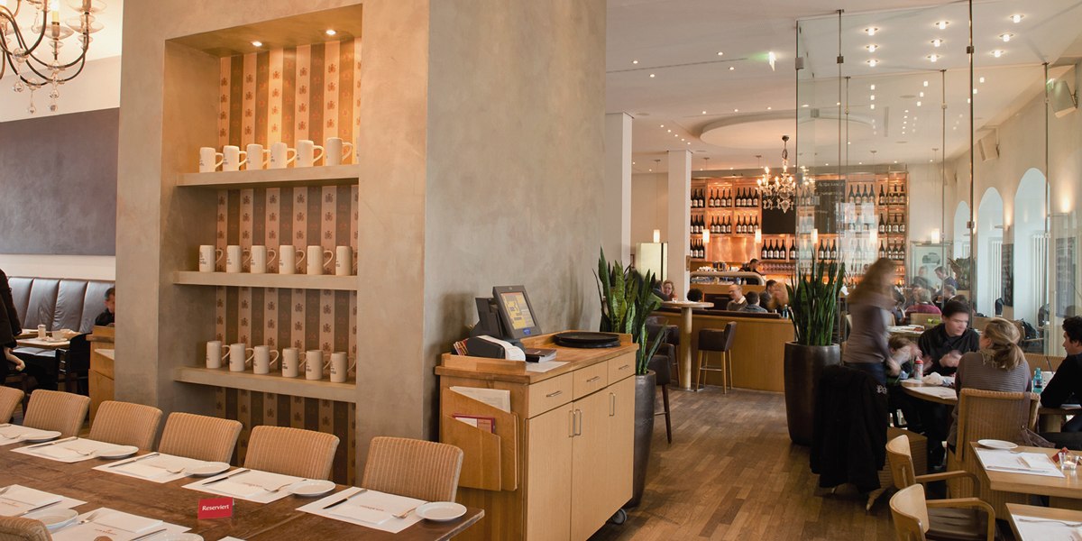 Stilvolles Restaurant mit Holzmöbeln, Regalen voller Tassen und einer gemütlichen Atmosphäre. Gäste sitzen an Tischen, im Hintergrund eine Bar., © Aspectus Photographie Stuttgart