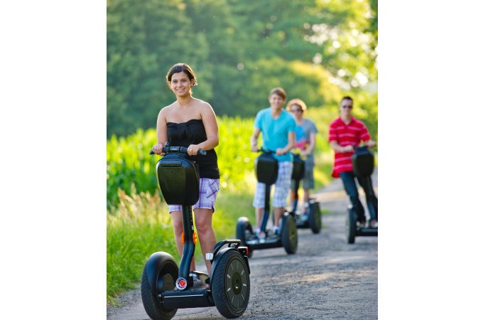 Vier Personen fahren auf Segways einen ländlichen Weg entlang, umgeben von grüner Natur und Bäumen im Hintergrund., © Cool-Tours StattReisen Vier Personen fahren auf Segways einen ländlichen Weg entlang, umgeben von grüner Natur und Bäumen im Hintergrund., © Cool-Tours StattReisen