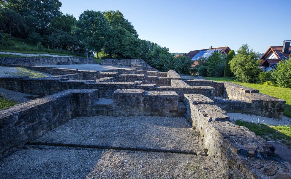 Ruinen der Villa Rustica in Nürtingen, umgeben von Bäumen und modernen Häusern im Hintergrund., © SMG, A. Mende