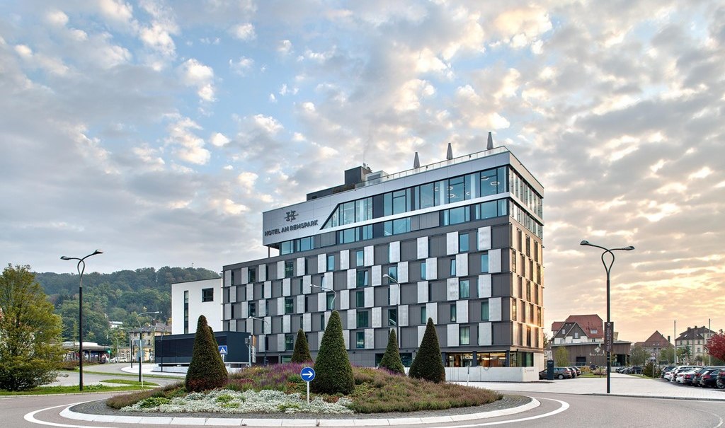 Modernes Hotelgebäude mit Glasfassade, umgeben von einem Kreisverkehr und gepflegter Landschaftsgestaltung, bei Sonnenuntergang., © Hotel am Remspark Modernes Hotelgebäude mit Glasfassade, umgeben von einem Kreisverkehr und gepflegter Landschaftsgestaltung, bei Sonnenuntergang., © Hotel am Remspark