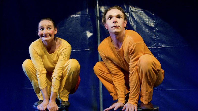 Zwei Personen in gelben und orangefarbenen Kost&uuml;men hocken auf Hockern vor einem blauen Hintergrund, wirken konzentriert und fr&ouml;hlich., &copy; Stadt Leinfelden-Echterdingen, Kulturamt