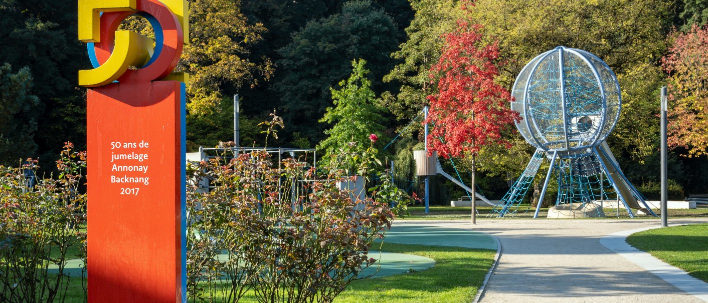 Ein Park mit einer bunten Skulptur und einem Spielplatz. Herbstbäume im Hintergrund, blauer Himmel mit Wolken., © René Straube
