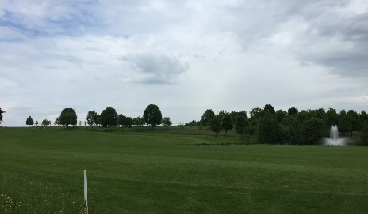 Ein weitl&auml;ufiger Golfplatz mit gr&uuml;ner Wiese, B&auml;umen und einem Springbrunnen im Hintergrund. Der Himmel ist bew&ouml;lkt., &copy; www.pro-cycl.de