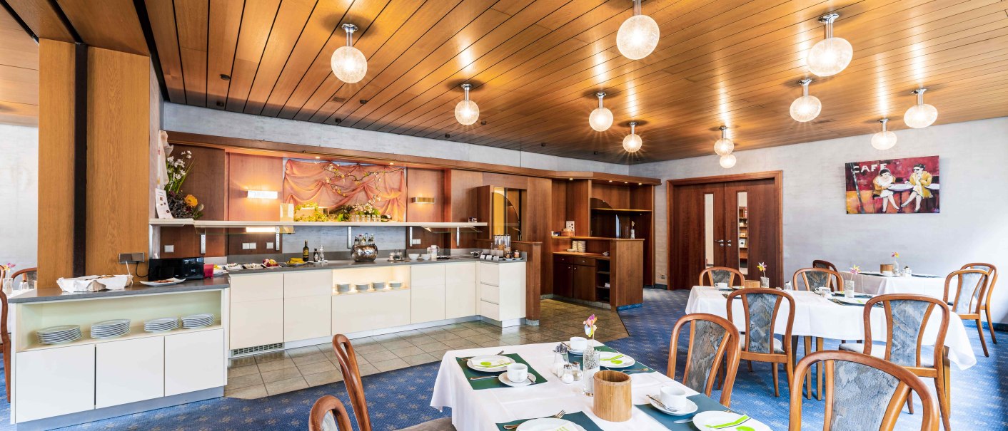 Elegantes Restaurant mit Holzelementen, gedeckten Tischen und Buffetstation. Warme Beleuchtung und gemütliche Atmosphäre., © TOMAS