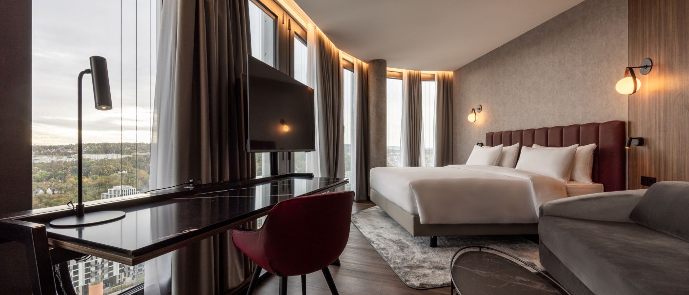 Moderne Hotelsuite mit großem Bett, Schreibtisch, Fernseher und Panoramafenster mit Blick auf die Stadt., © Radisson Hotel Group