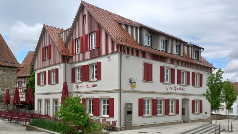 mehrstöckiges Gebäude mit hell verputzter Fassade und rötlich-braun holzverkleidetem Dachgeschoss, die zahlreichen weißgerahmten Sprossenfnster haben rot lackierte Klappläden, © Petra Natzkowski mehrstöckiges Gebäude mit hell verputzter Fassade und rötlich-braun holzverkleidetem Dachgeschoss, die zahlreichen weißgerahmten Sprossenfnster haben rot lackierte Klappläden, © Petra Natzkowski