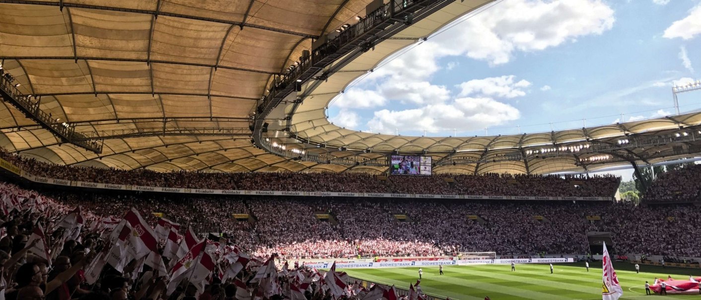 Die Mercedes-Benz Arena in Stuttgart, voll besetzt mit Fans, die Fahnen schwenken. Das Stadiondach ist gut sichtbar, der Himmel ist blau mit Wolken., © Stuttgart-Marketing GmbH Die Mercedes-Benz Arena in Stuttgart, voll besetzt mit Fans, die Fahnen schwenken. Das Stadiondach ist gut sichtbar, der Himmel ist blau mit Wolken., © Stuttgart-Marketing GmbH