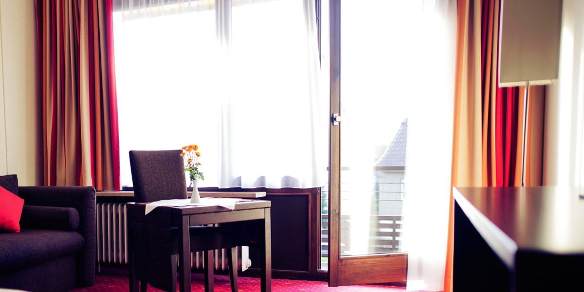 Helles Zimmer mit Tisch, Stühlen, Sofa und großem Fenster. Vorhänge in Rot- und Beigetönen, Blumen auf dem Tisch., © Hotel Sonne-Post Helles Zimmer mit Tisch, Stühlen, Sofa und großem Fenster. Vorhänge in Rot- und Beigetönen, Blumen auf dem Tisch., © Hotel Sonne-Post