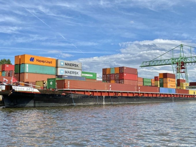 Ein Containerschiff im Stuttgarter Hafen mit bunten Containern und einem Kran im Hintergrund unter blauem Himmel., © Stuttgart Marketing GmbH