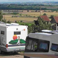Wohnmobile parken auf einem Stellplatz mit Blick auf eine weite Landschaft und Felder. Im Hintergrund sind Hügel und eine Stadt zu sehen., © PANORAMAWEINGUT Baumgärtner Wohnmobile parken auf einem Stellplatz mit Blick auf eine weite Landschaft und Felder. Im Hintergrund sind Hügel und eine Stadt zu sehen., © PANORAMAWEINGUT Baumgärtner