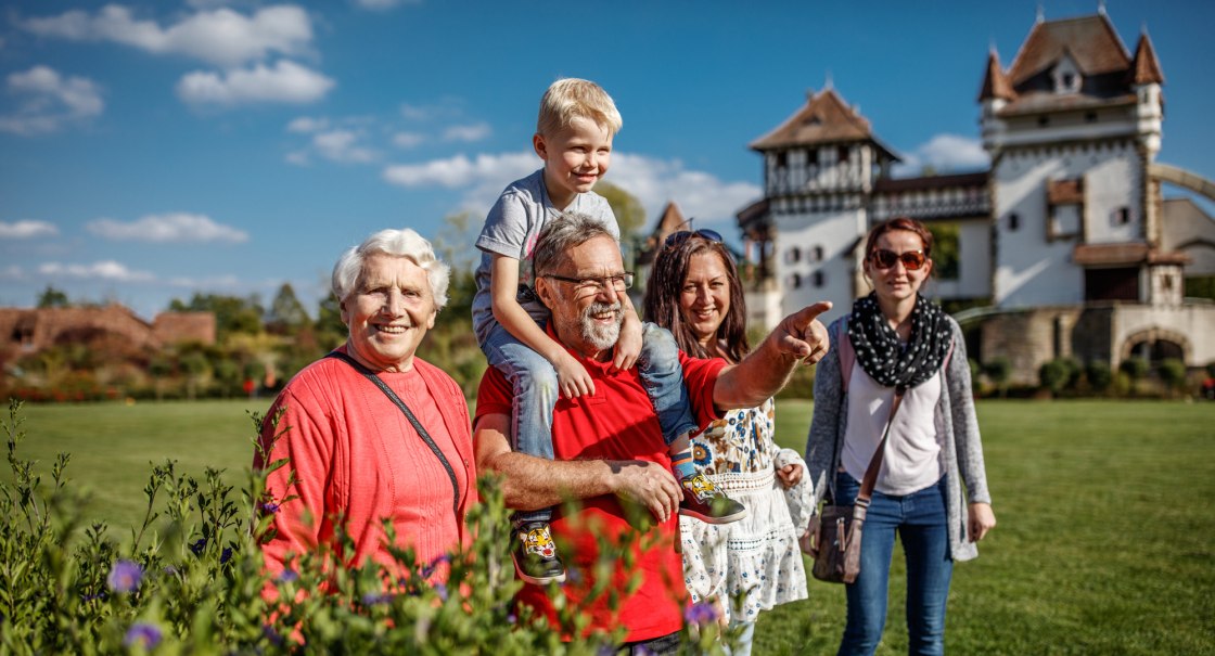 Eine fröhliche Familie posiert in einem Garten vor einem Schloss. Ein älterer Mann trägt ein Kind auf den Schultern und zeigt in die Ferne., © Erlebnispark Tripsdrill Eine fröhliche Familie posiert in einem Garten vor einem Schloss. Ein älterer Mann trägt ein Kind auf den Schultern und zeigt in die Ferne., © Erlebnispark Tripsdrill