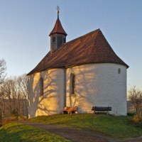 Die Marienkapelle in Wissgoldingen steht auf einem Hügel, beleuchtet von der Abendsonne. Bäume werfen Schatten auf die weiße Fassade., © Foto: Frieder Kopper