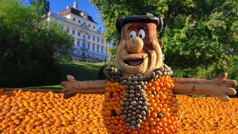 Eine große Kürbisfigur steht vor einem Schloss, umgeben von zahlreichen Kürbissen. Der Himmel ist klar und blau., © copyright: Marc Sansone Eine große Kürbisfigur steht vor einem Schloss, umgeben von zahlreichen Kürbissen. Der Himmel ist klar und blau., © copyright: Marc Sansone