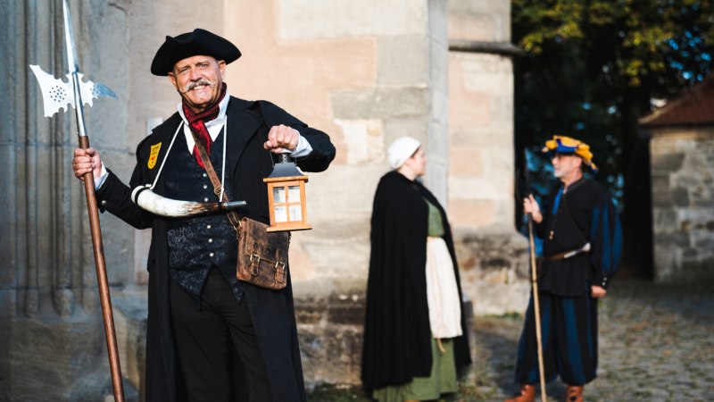 Ein Mann in historischer Kleidung mit Laterne und Hellebarde. Zwei weitere Personen in mittelalterlicher Kleidung im Hintergrund., © Stadt Nürtingen, U. Jendrass Ein Mann in historischer Kleidung mit Laterne und Hellebarde. Zwei weitere Personen in mittelalterlicher Kleidung im Hintergrund., © Stadt Nürtingen, U. Jendrass