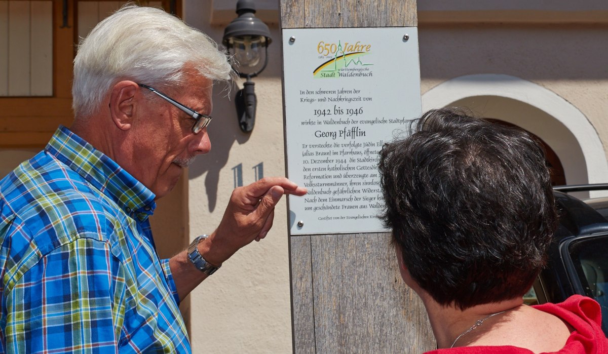 Zwei Personen lesen eine Gedenktafel an einem Holzpfosten. Die Tafel erinnert an historische Ereignisse in der Stadt Waldenbuch., © Natur.Nah. Schönbuch & Heckengäu