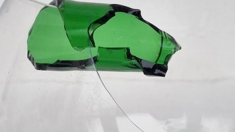 Ein zerbrochenes grünes Glasstück schwebt vor einem weißen Hintergrund. Die Kanten sind unregelmäßig und scharf., © Bettina Funke