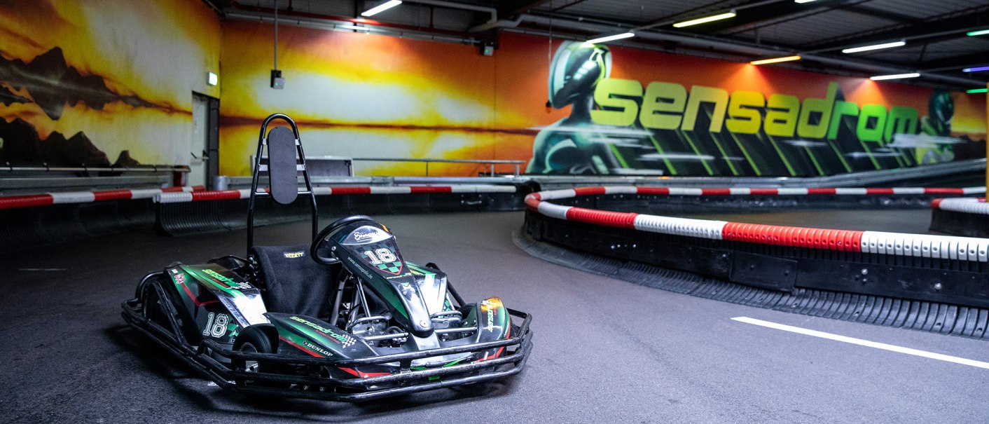 Ein Go-Kart steht auf einer Indoor-Kartbahn. An der Wand ist ein großes Graffiti mit dem Schriftzug 'Sensadrom' zu sehen., © Sensapolis GmbH Ein Go-Kart steht auf einer Indoor-Kartbahn. An der Wand ist ein großes Graffiti mit dem Schriftzug 'Sensadrom' zu sehen., © Sensapolis GmbH