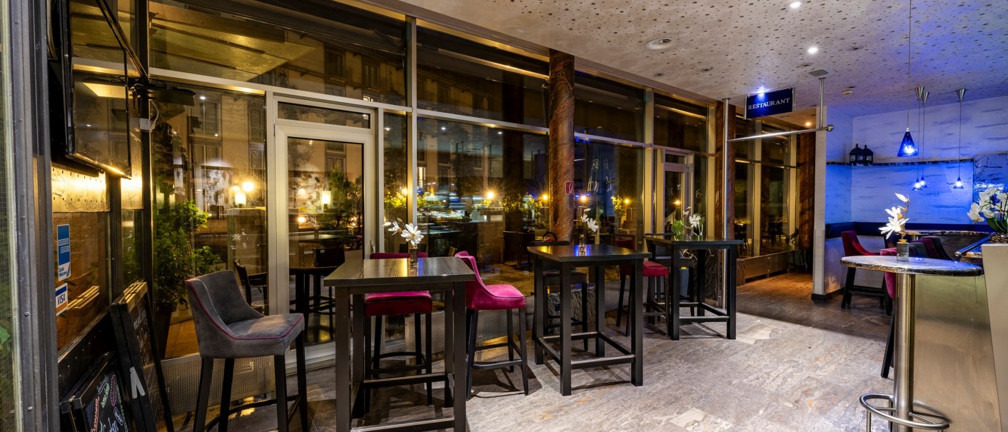 Moderne Bar mit hohen Tischen und Stühlen, dekoriert mit Blumenvasen. Große Fensterfront und dezente Beleuchtung bei Nacht., © Plaza Residence Stuttgart-Ditzingen Moderne Bar mit hohen Tischen und Stühlen, dekoriert mit Blumenvasen. Große Fensterfront und dezente Beleuchtung bei Nacht., © Plaza Residence Stuttgart-Ditzingen