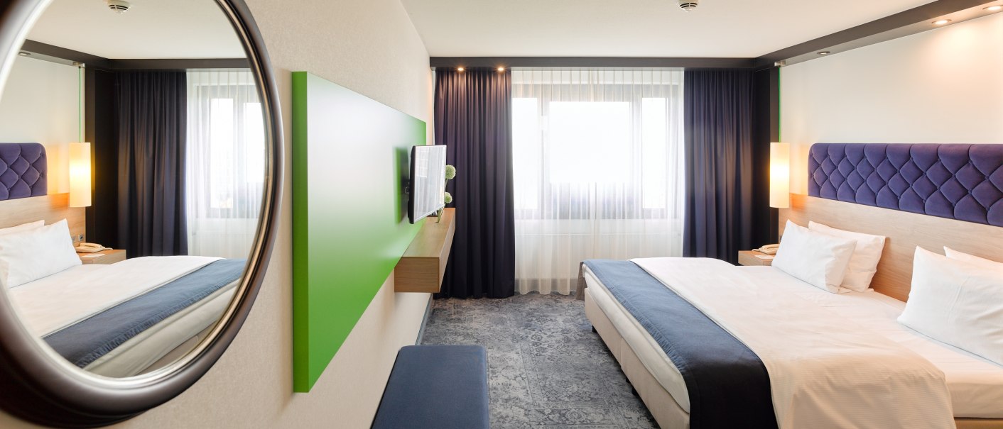 Modernes Hotelzimmer mit großem Bett, blauem Kopfteil, Spiegel, Fernseher und großen Fenstern mit Vorhängen., © Holiday Inn Stuttgart Modernes Hotelzimmer mit großem Bett, blauem Kopfteil, Spiegel, Fernseher und großen Fenstern mit Vorhängen., © Holiday Inn Stuttgart
