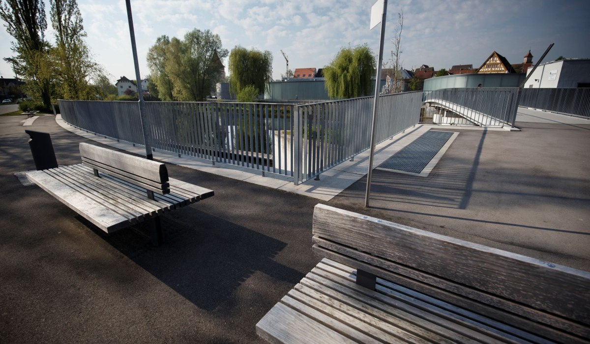 Moderne Brücke mit Metallgeländer, Holzbänken und Bäumen im Hintergrund. Klare, sonnige Atmosphäre mit leicht bewölktem Himmel., © Stoppel Moderne Brücke mit Metallgeländer, Holzbänken und Bäumen im Hintergrund. Klare, sonnige Atmosphäre mit leicht bewölktem Himmel., © Stoppel