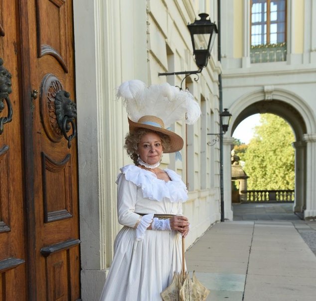 Eine Frau in einem eleganten, historischen Kost&uuml;m mit Hut und Feder steht vor einem Schloss. Sie h&auml;lt einen Sonnenschirm und l&auml;chelt in die Kamera., &copy; Fotograf: Reiner Pfisterer