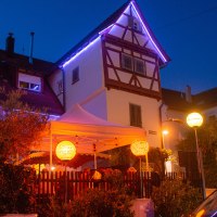 Ein beleuchtetes Fachwerkhaus mit einem weißen Zelt im Garten. Bunte Laternen und Lichterketten schaffen eine gemütliche Atmosphäre bei Nacht., © Weingut Ruoff