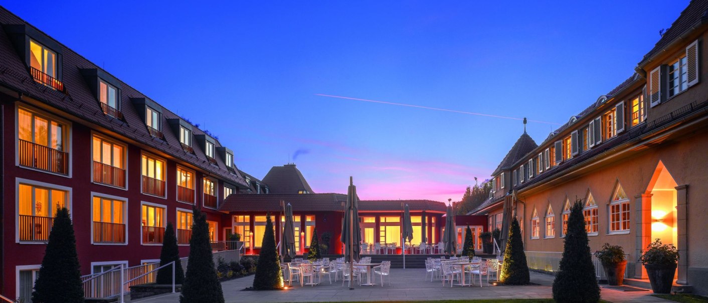 Das Waldhotel Stuttgart bei Dämmerung, mit beleuchteten Fenstern und einer Feuerstelle im Garten. Der Himmel ist blau mit einem rosa Streifen., © Waldhotel Stuttgart GmbH Das Waldhotel Stuttgart bei Dämmerung, mit beleuchteten Fenstern und einer Feuerstelle im Garten. Der Himmel ist blau mit einem rosa Streifen., © Waldhotel Stuttgart GmbH