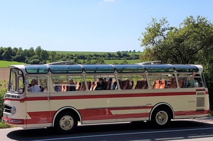 Ein Oldtimerbus mit Glasdach fährt durch eine ländliche Landschaft der Schwäbischen Alb. Der Himmel ist klar und blau., © SwabianTravel