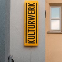 Ein gelbes Schild mit der Aufschrift 'KULTURWERK' hängt an einer Hauswand. Daneben ist ein Fenster und eine Uhr zu sehen., © Stuttgart-Marketing GmbH, Sarah Schmid Ein gelbes Schild mit der Aufschrift 'KULTURWERK' hängt an einer Hauswand. Daneben ist ein Fenster und eine Uhr zu sehen., © Stuttgart-Marketing GmbH, Sarah Schmid