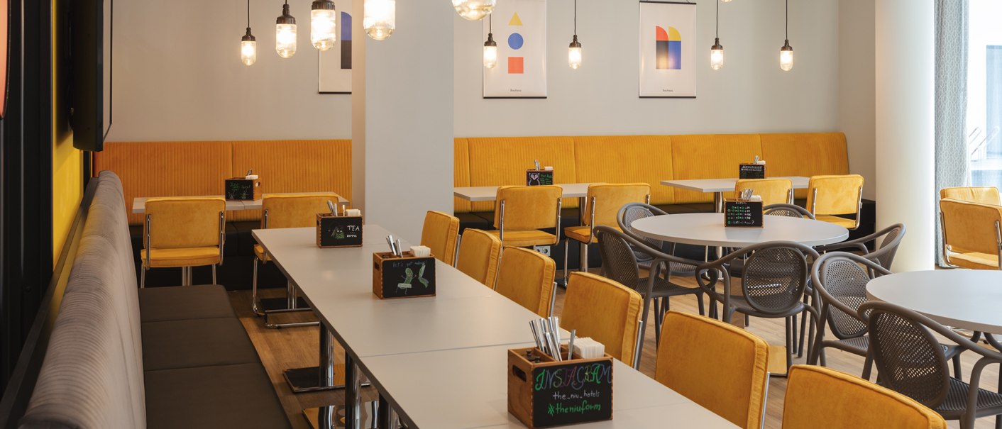Modernes Restaurant mit gelben Stühlen, Tischen und hängenden Lampen. Abstrakte Kunstwerke an den Wänden sorgen für eine stilvolle Atmosphäre., © the niu Form - Novum Hospitality