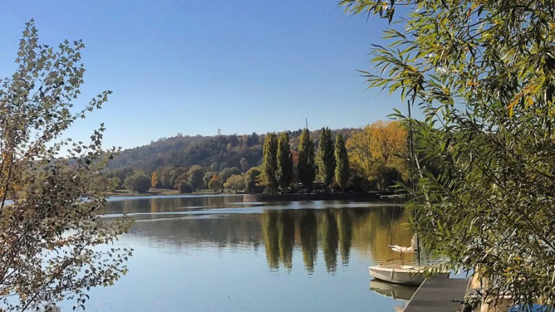 Der Max-Eyth-See mit ruhigem Wasser, umgeben von Bäumen. Ein Bootssteg und Boote sind am rechten Bildrand zu sehen., © Stuttgart-Marketing GmbH Der Max-Eyth-See mit ruhigem Wasser, umgeben von Bäumen. Ein Bootssteg und Boote sind am rechten Bildrand zu sehen., © Stuttgart-Marketing GmbH