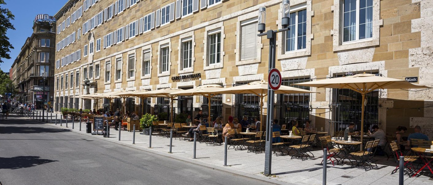 Carls Brauhaus mit Straßencafé, Sonnenschirmen und Gästen auf einer belebten Straße bei sonnigem Wetter., © SMG, Sarah Schmid Carls Brauhaus mit Straßencafé, Sonnenschirmen und Gästen auf einer belebten Straße bei sonnigem Wetter., © SMG, Sarah Schmid