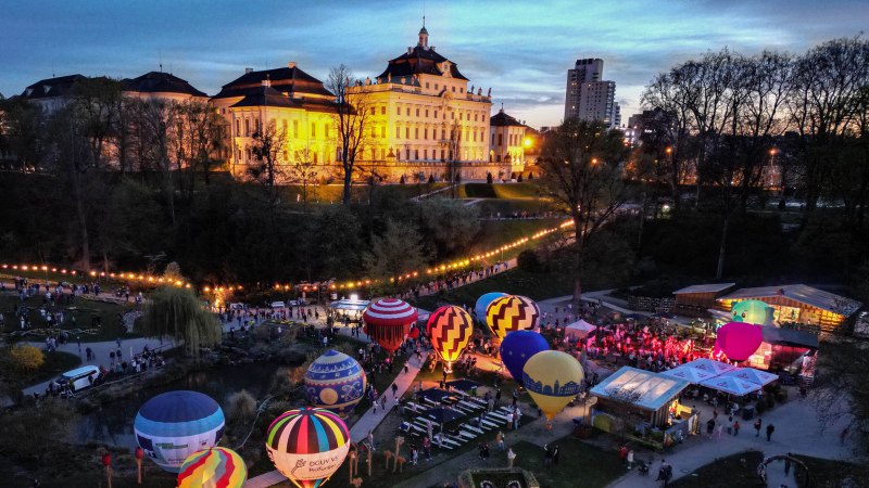 Hei&szlig;luftballons leuchten in der D&auml;mmerung vor einem hell erleuchteten Schloss. Menschen versammeln sich im Park, um das Spektakel zu beobachten., &copy; Dennis Straub