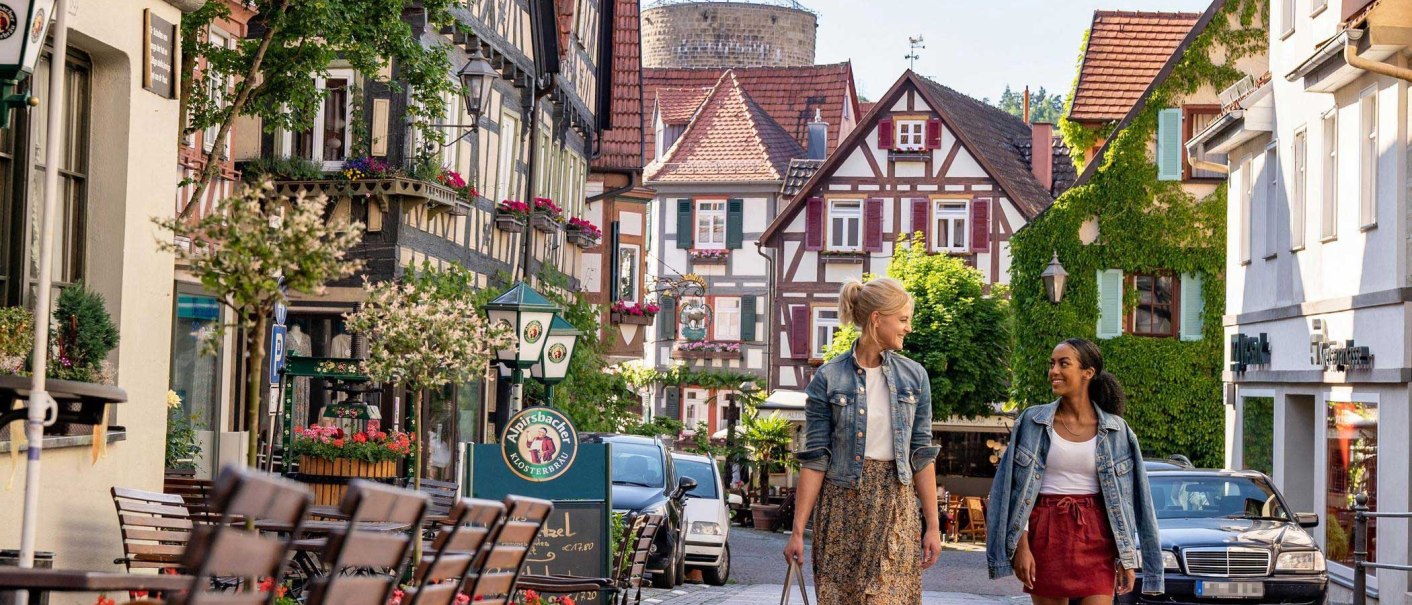 Blick die Kirchstraße mit ihren Fachwerkhäusern entlang auf den gemauerten Waldhornturm. Zwei Frauen flanieren durch die Straße., © SMG, Martina Denker
