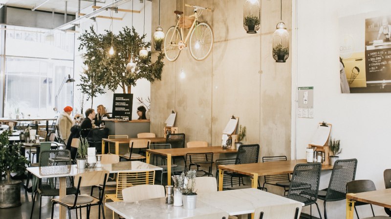 Modernes Caf&eacute; mit h&auml;ngendem Fahrrad an der Wand, Pflanzen und gem&uuml;tlichen Sitzbereichen. Menschen sitzen und unterhalten sich an Tischen., &copy; Claus Stuttgart