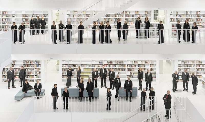 Eine Gruppe von Menschen in schwarzer Kleidung steht in einer modernen, weißen Bibliothek mit mehreren Etagen und Bücherregalen., © Schönblick gemeinnützige GmbH