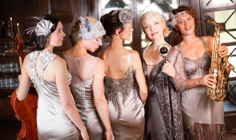 F&uuml;nf Frauen in eleganten, silbernen Kleidern der 1920er Jahre posieren mit Musikinstrumenten in einem stilvollen Raum. Sie verk&ouml;rpern den Glamour der Zeit., &copy; Touristik Bad Wildbad GmbH