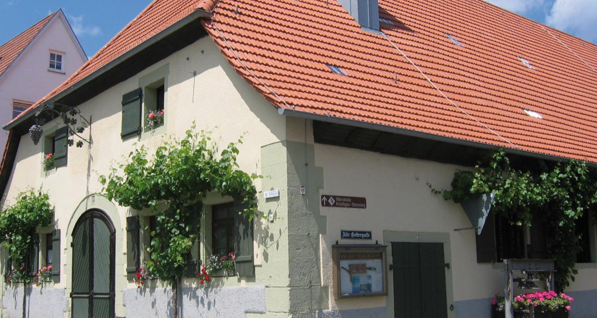 Historisches Gebäude mit rotem Ziegeldach, grünen Fensterläden und Weinreben an der Fassade. Ein Schild weist auf die "Alte Kelterstraße" hin., © Land der 1000 Hügel - Kraichgau-Stromberg Historisches Gebäude mit rotem Ziegeldach, grünen Fensterläden und Weinreben an der Fassade. Ein Schild weist auf die "Alte Kelterstraße" hin., © Land der 1000 Hügel - Kraichgau-Stromberg