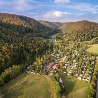 Luftaufnahme des Campingplatzes Pfählhof in einem bewaldeten Tal mit Wohnwagen und Zelten, umgeben von Hügeln und einer Straße., © Campingplatz Pfählhof Luftaufnahme des Campingplatzes Pfählhof in einem bewaldeten Tal mit Wohnwagen und Zelten, umgeben von Hügeln und einer Straße., © Campingplatz Pfählhof