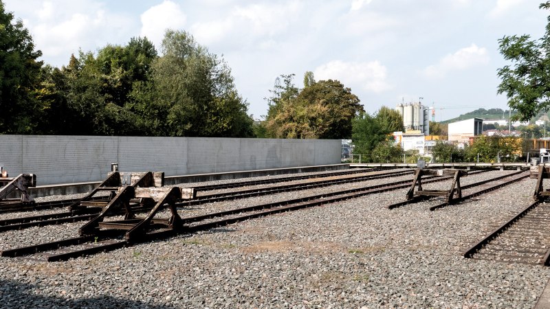 Gedenkstätte mit stillgelegten Bahngleisen, umgeben von Bäumen und einer Mauer. Ein ruhiger Ort des Erinnerns., © Foto-Kunst Andreas Keller Gedenkstätte mit stillgelegten Bahngleisen, umgeben von Bäumen und einer Mauer. Ein ruhiger Ort des Erinnerns., © Foto-Kunst Andreas Keller