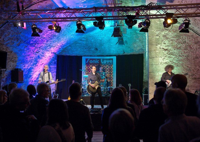 Band spielt in einem Gewölbekeller vor Publikum, bunte Lichter, Banner mit 'Sonic Love' im Hintergrund., © Theater im Schlosskeller Band spielt in einem Gewölbekeller vor Publikum, bunte Lichter, Banner mit 'Sonic Love' im Hintergrund., © Theater im Schlosskeller