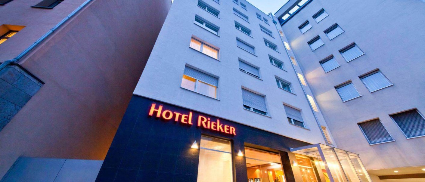 Das Hotel Rieker am Hauptbahnhof zeigt eine moderne Fassade mit beleuchtetem Eingang und großen Fenstern. Der Himmel ist klar und blau., © PLAZA INN Rieker Stuttgart Hauptbahnhof Das Hotel Rieker am Hauptbahnhof zeigt eine moderne Fassade mit beleuchtetem Eingang und großen Fenstern. Der Himmel ist klar und blau., © PLAZA INN Rieker Stuttgart Hauptbahnhof