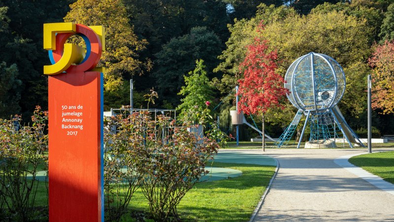 Ein Park mit einer bunten Skulptur und einem Spielplatz. Herbstbäume im Hintergrund, blauer Himmel mit Wolken., © René Straube