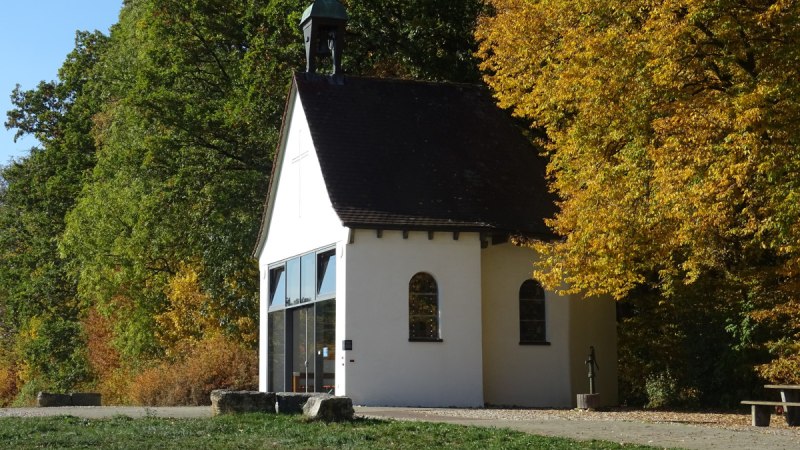 Weiße Kapelle mit Glockenturm, umgeben von herbstlich gefärbten Bäumen und grünem Rasen., © Foto: Cornelia Steinbach