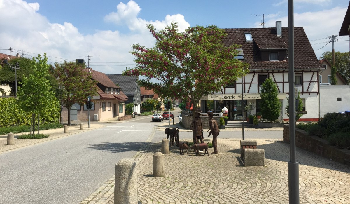 Straßenszene in Deckenpfronn mit Skulpturen von Menschen und Tieren auf einem gepflasterten Platz. Im Hintergrund ein Fachwerkhaus und ein Restaurant., © www.pro-cycl.de Straßenszene in Deckenpfronn mit Skulpturen von Menschen und Tieren auf einem gepflasterten Platz. Im Hintergrund ein Fachwerkhaus und ein Restaurant., © www.pro-cycl.de