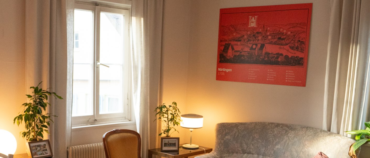 Ein gem&uuml;tliches Wohnzimmer mit antiken M&ouml;beln, darunter ein Sofa, ein runder Tisch und St&uuml;hle. An der Wand h&auml;ngt ein rotes Bild. Pflanzen und Lampen sorgen f&uuml;r Atmosph&auml;re., &copy; HerzoginN&uuml;rtingen