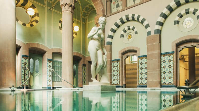 Historisches Schwimmbecken mit kunstvollen Fliesen und einer Statue in einem eleganten, gewölbten Raum., © ©LOCHER Fotodesign & Manufaktur ©Staatsbad Wildbad GmbH Historisches Schwimmbecken mit kunstvollen Fliesen und einer Statue in einem eleganten, gewölbten Raum., © ©LOCHER Fotodesign & Manufaktur ©Staatsbad Wildbad GmbH