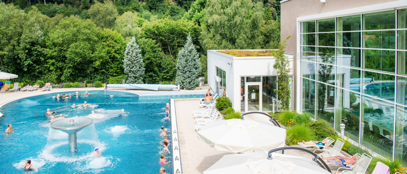 Außenpool der Paracelsus-Therme in Bad Liebenzell, umgeben von Wald. Menschen entspannen im Wasser und auf Liegestühlen. Moderne Architektur mit großen Fenstern., © Locher Fotodesign & Manufaktur Außenpool der Paracelsus-Therme in Bad Liebenzell, umgeben von Wald. Menschen entspannen im Wasser und auf Liegestühlen. Moderne Architektur mit großen Fenstern., © Locher Fotodesign & Manufaktur